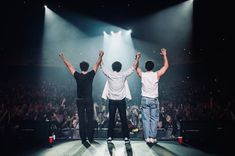 three men standing on stage with their arms in the air and hands raised above them