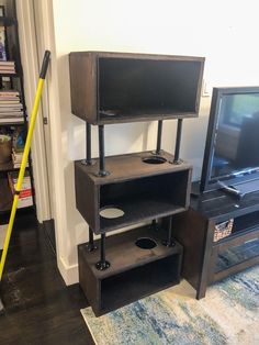 an entertainment center with a television on top of it and a broom leaning against the wall