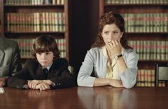 three people sitting at a table in front of bookshelves with one person covering his mouth