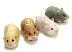 three small stuffed animals are lined up in a row on a white surface, with one hamster looking at the camera