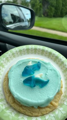 a cookie with blue icing sitting on top of a plate in front of a car