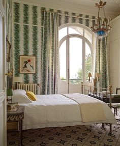 a bedroom with a bed, chair and chandelier in front of a large window