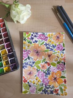 a painting with flowers and watercolors next to some paintbrushes on a table