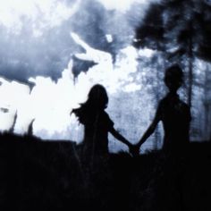 two people holding hands in front of a dark sky with trees and clouds behind them