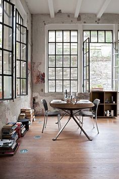 a dining room table and chairs in front of large windows with books on the floor