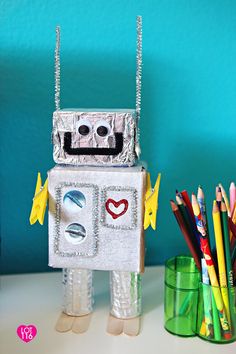 a robot made out of tinfoil and colored pencils next to a cup full of crayons