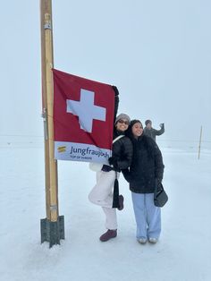 two women standing next to a swiss flag on top of a snow covered field in the middle of winter