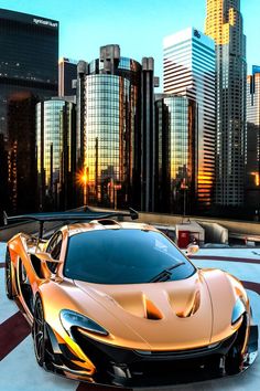 an orange sports car is parked in front of some tall buildings and the sun sets