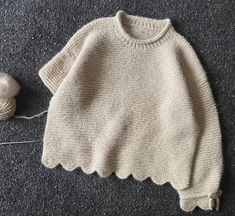 a knitted sweater sitting next to a ball of yarn and a knitting needle on the floor