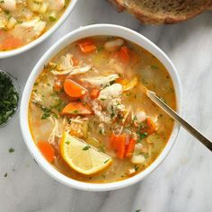 two bowls filled with chicken and vegetable soup next to some bread on a marble surface