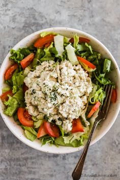 a white bowl filled with salad on top of a gray table next to a fork