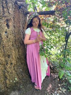 a girl in a pink dress leaning against a tree