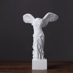 a white statue with wings on top of a wooden table