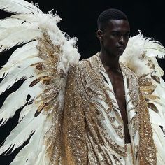 a man with white and gold feathers on his shoulders, wearing a golden jacket that is draped over his shoulder