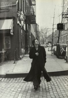 an old photo of a man walking down the street with his coat over his shoulders