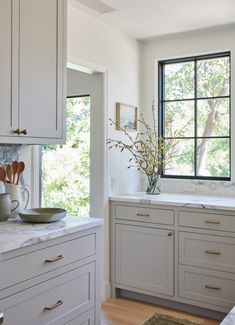 a kitchen with white cabinets and marble counter tops is pictured in this image, there are plants on the window sill