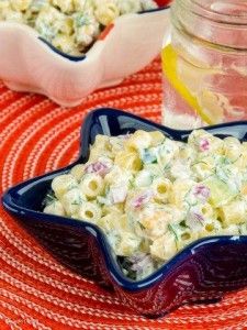 a blue bowl filled with macaroni salad on top of a red and white table cloth