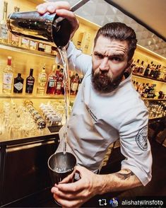 a man pouring something into a cup in front of a shelf full of liquor bottles