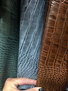 a hand is holding an item in front of several different colored alligator skin leathers