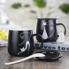 two black coffee mugs sitting on top of a wooden table next to a spoon