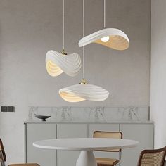 three lights hanging from the ceiling above a table with chairs and a round white table