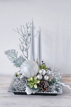 an arrangement of silver and white decorations on a tray with two candles in the center