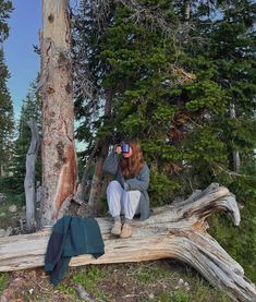 a woman sitting on top of a fallen tree next to a forest filled with trees