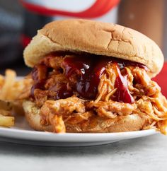 a pulled pork sandwich with bbq sauce and french fries on a white plate next to a bottle of ketchup