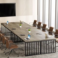 a conference table with chairs and laptops in front of a flat screen tv mounted on the wall