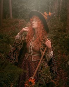 a woman with red hair wearing a witches hat and holding a stick in the woods