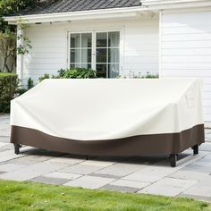 an outdoor couch covered in a white and brown cover next to a brick patio area