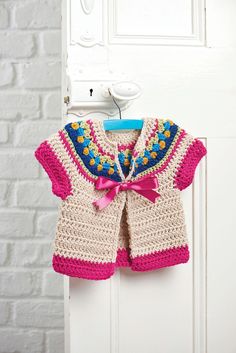 crocheted baby sweaters and balls of yarn are shown in three different colors