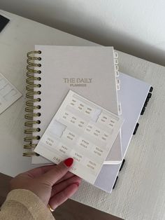 a hand holding a planner next to a notebook with the daily planner on top of it