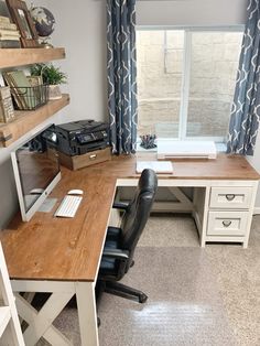 a desk with a computer on top of it in front of a window and bookshelf