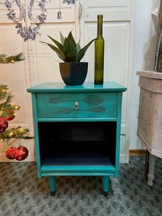 a blue table with a green vase and a bottle on it next to a christmas tree