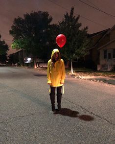 a person wearing a yellow raincoat and holding a red balloon in the middle of an empty street