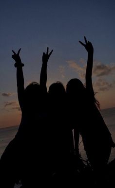 two girls are standing in front of the ocean with their hands up and arms raised