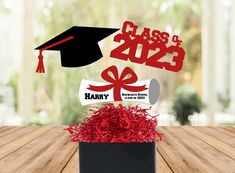 a graduation cap and tassel on top of a box filled with red shredded paper