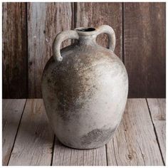 an old gray vase sitting on top of a wooden table next to a wood wall