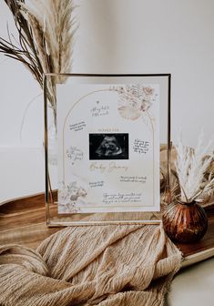 a photo frame sitting on top of a wooden table next to dried plants and a vase