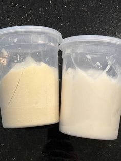 two plastic containers filled with white liquid sitting on top of a black counter next to each other