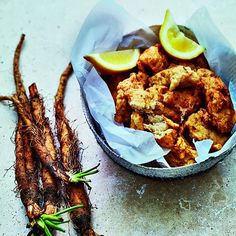 a bowl filled with fried food next to two lemon wedges and some carrots