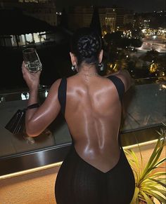 a woman in a black swimsuit holding a wine glass and looking at the city