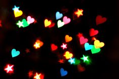 many different colored hearts and stars on a black background with blurry lights in the foreground