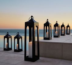 several black and white lanterns sitting on top of a cement wall near the ocean at sunset