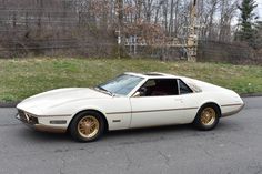 a white sports car parked on the side of the road in front of some trees