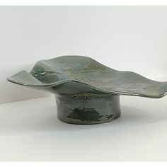 a metal bowl with a leaf shaped design on the top and bottom, sitting on a white surface