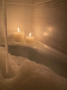 two candles are lit in the bathtub next to each other and water is flowing from the faucet