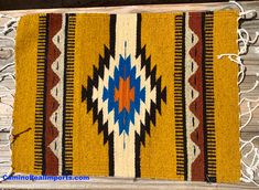 a yellow and blue rug with fringes on top of wooden flooring next to wall