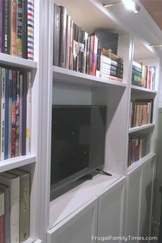 a bookshelf filled with lots of books next to a flat screen tv on top of a white book shelf